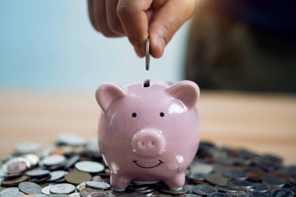 A kid puts a coin into a piggy bank.