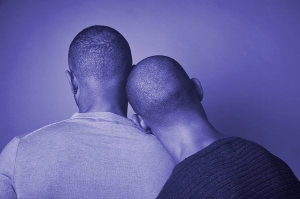 Photo of two Black men, with one resting his head on the other's shoulder