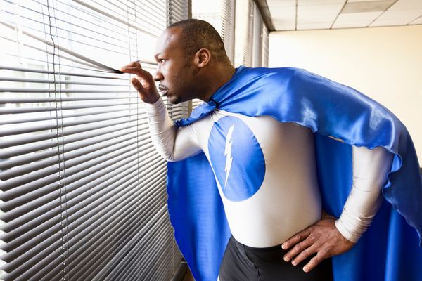 Black man in superhero costume looks out window